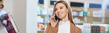 Foto de Mujer alegre de buen aspecto en traje de moda hablando por teléfono, mientras que en la tienda de cosméticos, bandera - Imagen libre de derechos