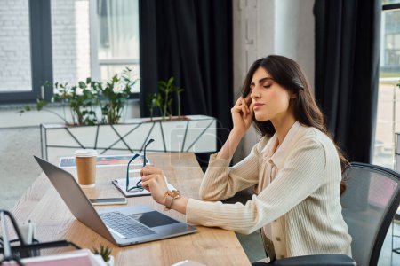 Une femme d'affaires est assise à une table, concentrée sur son ordinateur portable dans un espace de travail de bureau moderne, incarnant le concept de franchise.