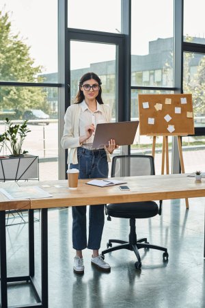 Eine Geschäftsfrau steht selbstbewusst an ihrem modernen Bürotisch, konzentriert auf ihren Laptop, der das Franchise-Konzept symbolisiert.