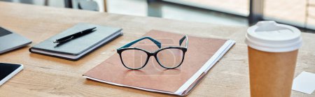 A pair of glasses rests on a vibrant notebook next to a steaming cup of coffee, set in a modern office workspace.