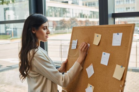 A dynamic female entrepreneur stands confidently in front of a board filled with strategic plans and ideas in a modern office space.