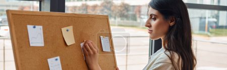 Téléchargez les photos : Une femme d'affaires explore un babillard orné de notes post-it colorées dans un espace de travail moderne. - en image libre de droit