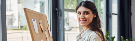 A businesswoman stands poised in front of a wooden board, fully immersed in her artistic endeavor within a modern office workspace.