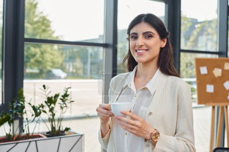 Photo for A businesswoman savors a cup of coffee against a cityscape backdrop through a large window in a modern office. - Royalty Free Image