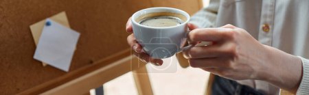 Eine moderne Geschäftsfrau macht in ihrem Büro eine Kaffeepause und hält eine Tasse frisch gebrühten Kaffee in der Hand.