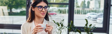 A stylish woman in glasses enjoys a cup of coffee in a modern office, with a hint of focus on productivity and relaxation.