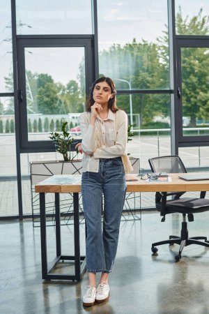 A modern businesswoman stands confidently in front of a sleek table in a contemporary office setting.