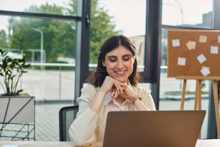 Eine Geschäftsfrau sitzt in einem modernen Büro vor einem Laptop und konzentriert sich auf ihre Franchise-Konzeptarbeit.