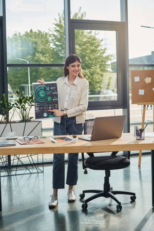 Eine Geschäftsfrau steht in einem modernen Büro, konzentriert sich auf ihren Laptop an einem stilvollen Schreibtisch und präsentiert das Franchise-Konzept.