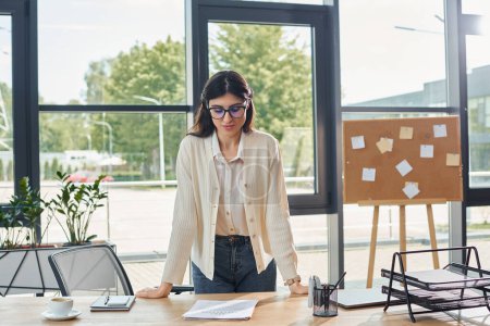 A businesswoman standing confidently in front of a sleek wooden table in a modern office workspace.