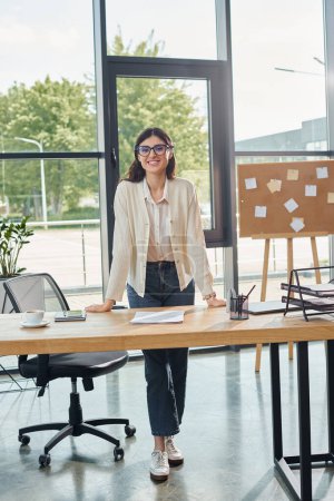 Une femme d'affaires se tient confiante dans un bureau moderne, devant un bureau, incarnant le concept de franchise.