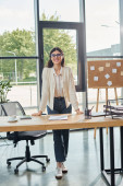 A businesswoman stands confidently in a modern office, in front of a desk, embodying the franchise concept. Stickers #697225708