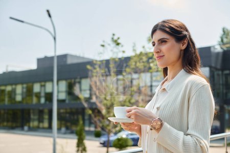 Téléchargez les photos : Une femme d'affaires tenant une tasse de café devant un immeuble de bureaux moderne. - en image libre de droit