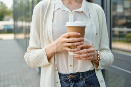 A businesswoman enjoys a quiet moment outdoors, holding a cup of coffee.