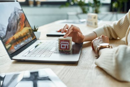 Una empresaria moderna sostiene un modelo de casa pequeña frente a un ordenador portátil, encarnando la innovación en los conceptos de franquicia.