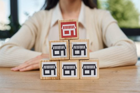 Photo for A determined businesswoman sits at a table, focused on arranging a stack of blocks, symbolizing her strategic approach to growing a franchise. - Royalty Free Image