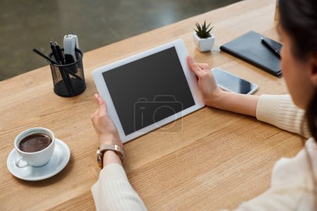Foto de Una sofisticada empresaria se sienta en una mesa, absorta en su trabajo en una tableta en un entorno de oficina moderno. - Imagen libre de derechos