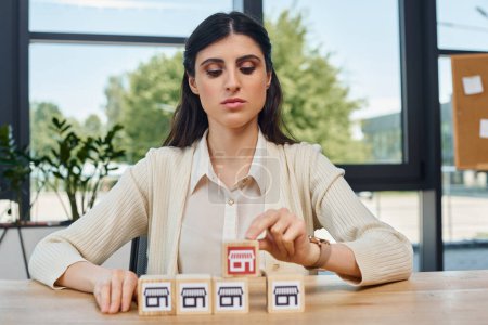 A determined businesswoman sits at a table, strategically arranging blocks as part of a franchise concept in a modern office.