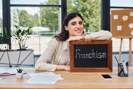 Eine Geschäftsfrau sitzt an einem modernen Schreibtisch und zeigt ein Schild als Symbol ihrer unternehmerischen Bemühungen..