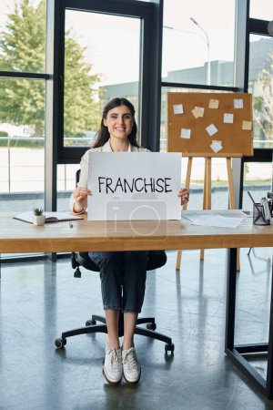 A modern businesswoman sitting at a desk, holding a sign with determination.