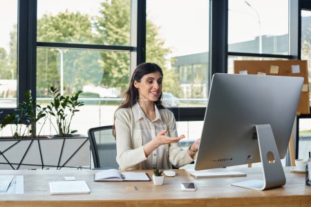 Une femme d'affaires est profondément concentrée alors qu'elle est assise à un bureau avec un ordinateur dans un environnement de bureau moderne.