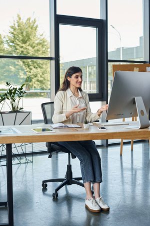 Eine Geschäftsfrau sitzt an einem Schreibtisch in einem modernen Büro und arbeitet an einem Computer.