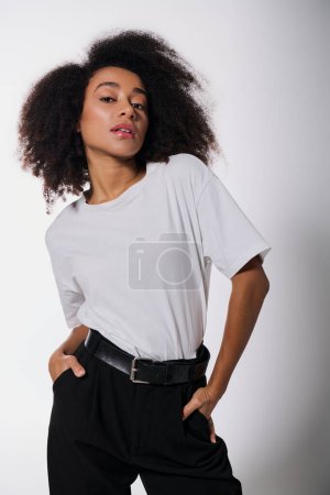 atractiva mujer afroamericana posando con las manos en los bolsillos y mirando a la cámara, concepto de moda