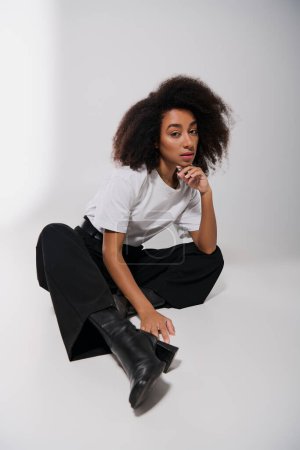 appealing african american female model sitting on floor and looking at camera, fashion concept