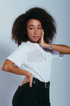 beautiful african american woman in chic attire with curly hair looking at camera, fashion concept mug #697415724
