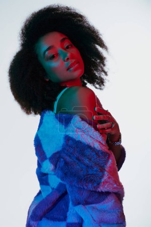 beautiful african american woman in vibrant faux fur with curly hair looking at camera in lights