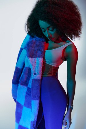 alluring stylish african american female model in fashionable faux fur looking way in lights