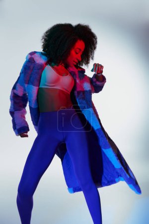 alluring stylish african american female model in fashionable faux fur looking way in lights