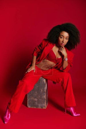 appealing sexy african american woman in red attire sitting and looking at camera, fashion concept