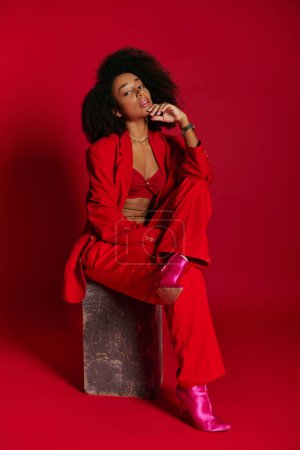 hermosa mujer afroamericana sexy en traje rojo sentado y mirando a la cámara, concepto de moda