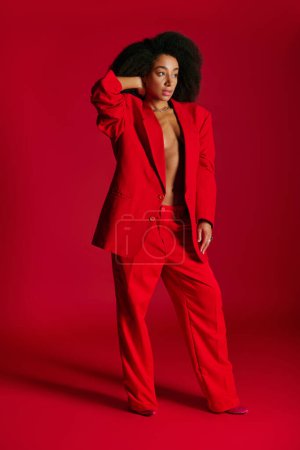 alluring african american female model in red blazer looking away on red background, fashion concept
