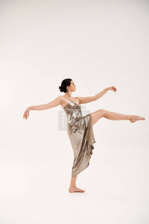 Foto de Una joven mujer exuda gracia y elegancia mientras baila en un vestido largo y brillante de plata en un ambiente de estudio sobre un fondo blanco. - Imagen libre de derechos
