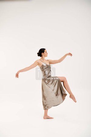 Eine junge Frau in einem silbernen Kleid tanzt anmutig in einem Studio-Setting und präsentiert Eleganz und Bewegung.