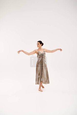 A young woman in a silver dress gracefully dances, expressing elegance and movement in a studio setting against a white backdrop.