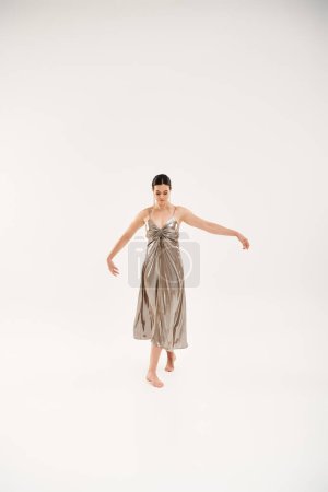 Eine junge Frau tanzt elegant in einem fließenden silbernen Kleid.