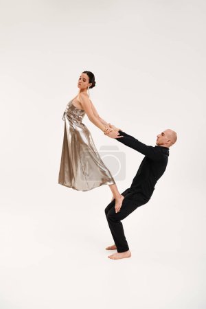A young man in black and a woman in a silver dress perform acrobatic dance moves together against a white studio background.
