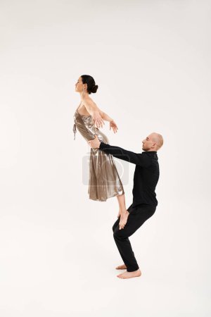 Joven hombre y mujer vestidos de negro realizando movimientos acrobáticos de baile en un piso blanco en un entorno de estudio.