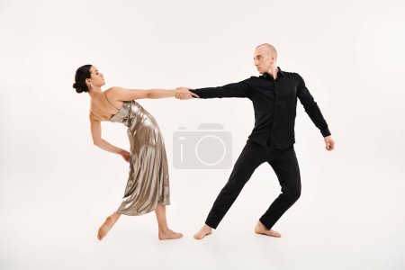 A young man in black and a young woman in a shiny silver dress showcasing acrobatic dance moves in a studio against a white background.