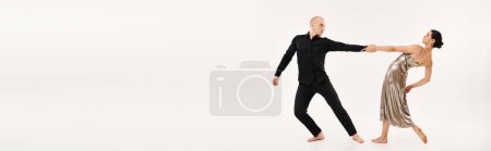 Photo for Young man in black and woman in silver dress joyfully dancing together, showcasing acrobatic elements in a studio shot on a white background. - Royalty Free Image