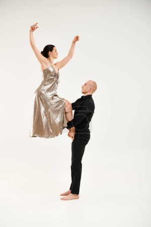 Young man in black and woman in shiny dress perform an acrobatic dance, with the man holding the woman.