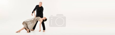 Ein junger Mann in Schwarz und eine junge Frau in einem glänzenden Kleid führen akrobatische Elemente vor, während sie in einem Studio auf weißem Hintergrund tanzen.