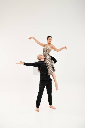 A young man in black carries a young woman in a dress while dancing gracefully, showcasing acrobatic elements.