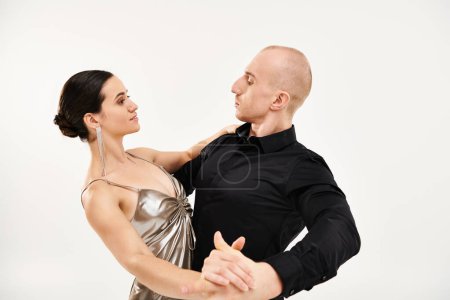 Ein junger Mann in Schwarz und eine junge Frau in einem glänzenden Kleid tanzen gemeinsam in einem Studio vor weißem Hintergrund..
