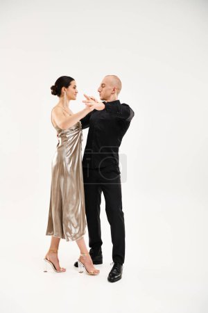 A young man in black and a young woman in a long shiny dress performing against a white background.