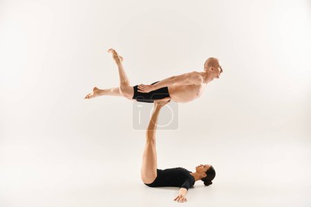 Shirtless young man and woman in black performing acrobatic elements.