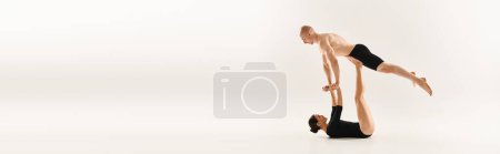 Shirtless young man and woman performing synchronized handstands in a studio setting against a white background.